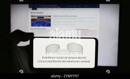 Stoccarda, Germania, 05-21-2024: Persona che detiene un cellulare con il logo del tribunale internazionale Corte europea dei diritti dell'uomo (CEDU) di fronte alla pagina web. F Foto Stock