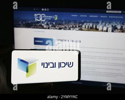 Stoccarda, Germania, 07-10-2024: Persona con smartphone con logo della società israeliana di sviluppo Shikun e Binui davanti al sito web. Concentrati sul phon Foto Stock