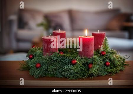 Primo Avvento, corona verde con baule natalizie, biscotti alla cannella e candele rosse, uno acceso, su un tavolo nel soggiorno, spazio copia, selec Foto Stock