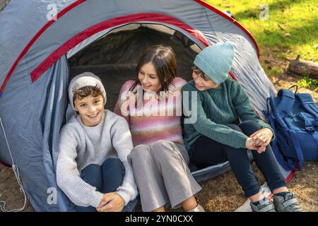 Vista ad angolo alto di tre fratelli sorridenti seduti sulla tenda da campeggio godendosi la natura Foto Stock