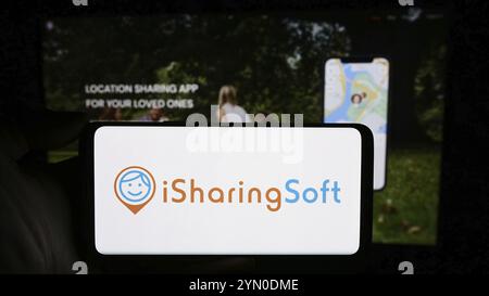 Stoccarda, Germania, 02-24-2024: Persona che detiene un cellulare con il logo della società americana di social mapping iSharingSoft Inc. (ISharing) di fronte alla pagina web Foto Stock