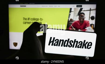 Stoccarda, Germania, 06-03-2024: Persona che detiene un telefono cellulare con il logo della società statunitense di software per il reclutamento Stryder Corp. (Handshake) di fronte alla pagina web Foto Stock