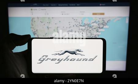 Stoccarda, Germania, 03-05-2024: Persona che tiene un cellulare con il logo della compagnia di autobus a lunga percorrenza Greyhound Lines Inc. Di fronte alla pagina web aziendale. Foto Stock