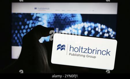 Stoccarda, Germania, 05-22-2024: Persona che detiene un telefono cellulare con il logo della società tedesca di media Holtzbrinck Publishing Group di fronte alla business web pa Foto Stock