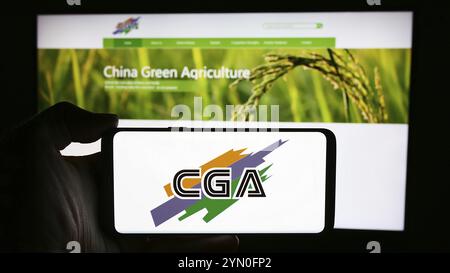 Stoccarda, Germania, 04-28-2024: Persona che detiene il cellulare con il logo della società cinese China Green Agriculture Inc. (CGA) di fronte alla pagina web aziendale. Foto Stock