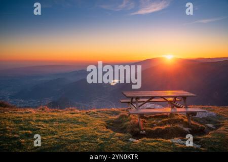 A stunning sunset casts vibrant colors over Mount Pizzoc in Cansiglio area in Veneto as the sun dips behind the mountains Foto Stock