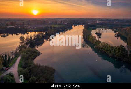 Un vivace tramonto proietta sfumature dorate sul fiume Sile, che si riflettono sulle sue acque calme. Vegetazione lussureggiante e sentieri tortuosi fiancheggiano le rive del fiume. Foto Stock