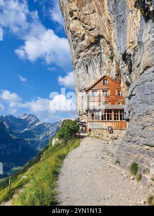 Ebenalp in Svizzera, Appenzell giugno 2021, Una pittoresca loggia in legno si erge precariamente contro una parete rocciosa a picco, circondata da montagne maestose e da un cielo azzurro. Foto Stock