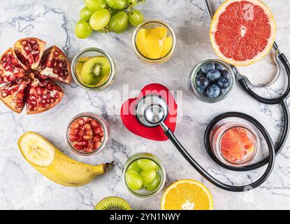 Frutti antiossidanti e antitumorali: Uva, kiwi, mirtilli, banana, pompelmo, arancia, melograno. Uno stetoscopio nasconde un cuore rosso. Prevenzione di h Foto Stock