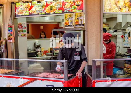 Venditore ambulante che prepara sapientemente la prelibatezza locale di Osaka - takoyaki, snack giapponese a forma di palla, fatto di farina di grano, ripieno di octo tritato o tagliato a dadini Foto Stock