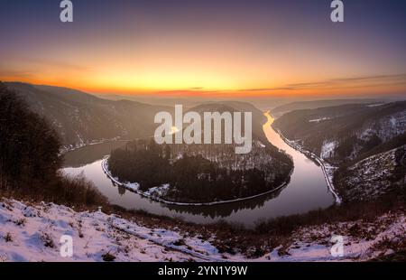 Una splendida vista panoramica di un fiume che si snoda attraverso una valle innevata al tramonto Foto Stock