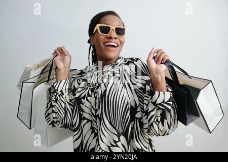 Donna sorridente che tiene in mano borse della spesa e indossa occhiali da sole Foto Stock