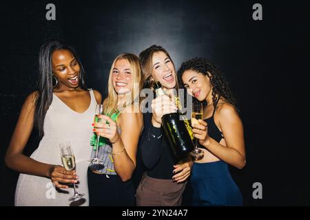 Un gruppo gioioso di quattro amici che festeggiano con champagne a una festa vivace. Stanno ridendo e si godono una serata di festa insieme, incarnando happ Foto Stock