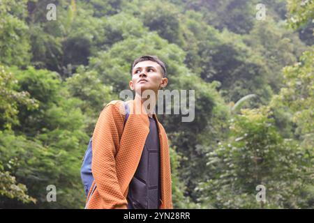 Ritratto di giovane uomo asiatico che viaggia in mezzo alla foresta. Uomo sicuro di sé che si guarda intorno mentre cammina nella natura con eccitanti espressioni Foto Stock