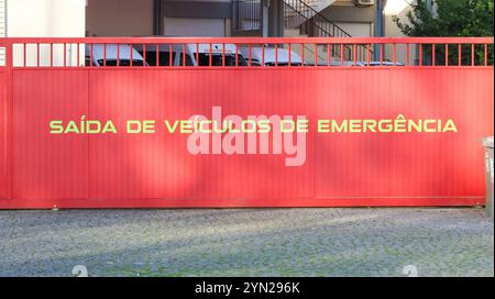 Cancello scorrevole rosso con l'iscrizione portoghese saida de veiculos de emergencia che indica l'uscita per i veicoli di emergenza Foto Stock