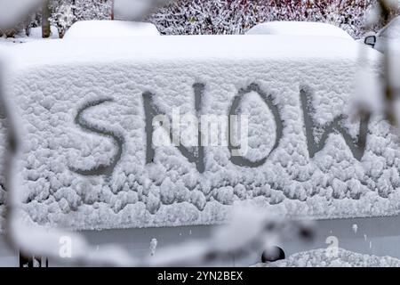 L'attacco dell'inverno, la prima nevicata, la parola neve scritta sul corpo dell'auto nella neve Foto Stock