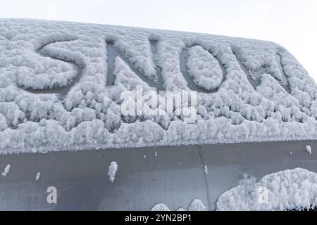 L'attacco dell'inverno, la prima nevicata, la parola neve scritta sul corpo dell'auto nella neve Foto Stock