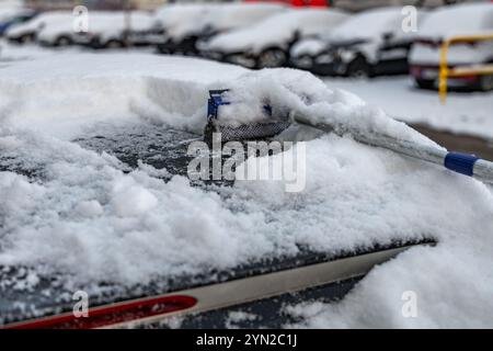 Una donna spara la neve dalla macchina, rimuovendo il ghiaccio dal corpo della macchina, attaccando l'inverno, preparando la macchina per il percorso Foto Stock