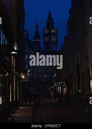 Incrocio tra Rue du cure Saint-Etienne e Rue Lepelletier, con la torre dell'orologio di le Palais De la Bourse davanti, Lille di notte Foto Stock