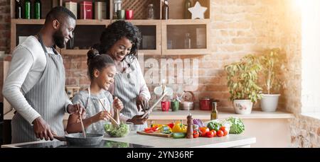 Mamma, papa' e figlia leggono la ricetta sul tablet in cucina Foto Stock