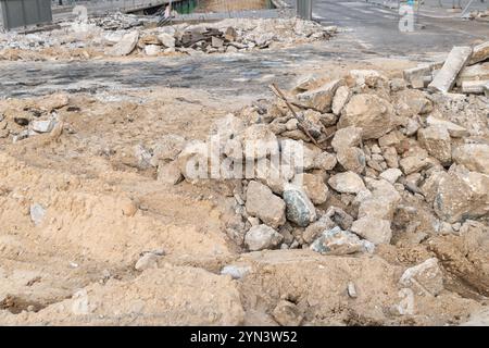 Un cantiere caratterizzato da un mucchio di macerie e sabbia, con pezzi di cemento rotti e armature esposte. Lo sfondo mostra un'ar parzialmente demolita Foto Stock