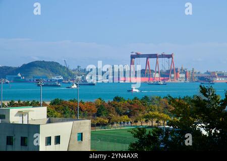 Ulsan, Corea del Sud - 14 novembre 2024: Le barche navigano nelle vivaci acque di fronte ai moli della Hyundai Heavy Industries, con gru e indust torreggianti Foto Stock