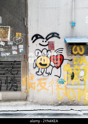 Playful Street Graffiti sulla Urban Wall di Hong Kong, vibrante Street Art con motivi Smiley e cuore Foto Stock