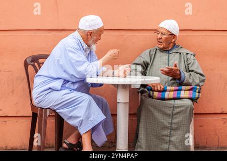 Ai piedi di un muro rosso, due uomini seduti a un tavolo discutono con gesti forti. Foto Stock