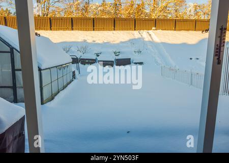 Cortile coperto di neve con serra, fioriere e recinzione in legno sotto la luce soffusa del mattino invernale. Foto Stock