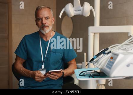 Ritratto di dentista maturo che indossa fischio mentre tiene in mano il telefono Foto Stock