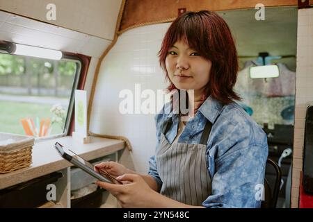 Ritratto di una giovane lavoratrice asiatica del camion alimentare con un tablet in mano sorridente e guardando la macchina fotografica Foto Stock