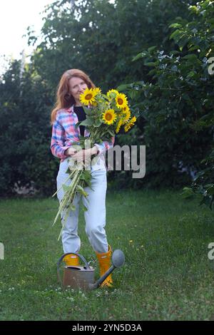 ragazza che tiene un mazzo enorme di girasoli nelle loro mani sullo sfondo di un paesaggio rurale Foto Stock