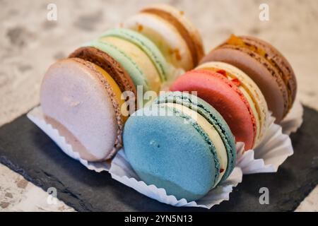 Un vivace assortimento di macaron colorati esposti su un piatto di ardesia. Perfetto per dessert, pasticceria francese e prelibatezze gourmet Foto Stock