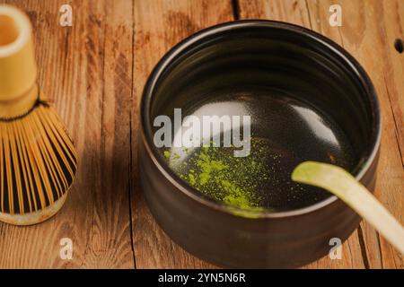 Una ciotola nera di matcha si trova su un tavolo di legno. La polvere verde viene versata nel recipiente del caffè matcha Foto Stock