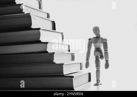 Uomo in legno a una gamba e libri come gradini, superare gli ostacoli, le difficoltà lungo il cammino, il cammino verso il successo attraverso le difficoltà Foto Stock