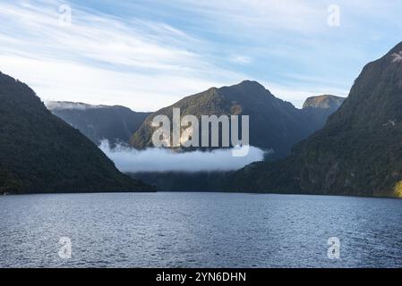 Sole che sorge su Doubtful Sound, nuvole che pendono in basso sulle montagne, Isola del Sud della Nuova Zelanda Foto Stock