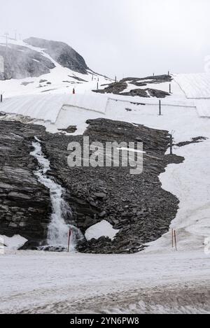 Una grande tela bianca che protegge il ghiaccio del ghiacciaio Hintertux nelle Alpi, una cascata di acqua sciolta scorre lungo la roccia, Austria, Europa Foto Stock