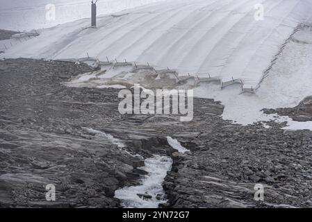 Una grande tela bianca che protegge il ghiaccio del ghiacciaio Hintertux nelle Alpi, una cascata di acqua sciolta scorre lungo la roccia, Austria, Europa Foto Stock