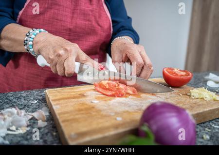 Primo piano delle mani di una donna adulta che taglia un pomodoro su un tagliere per una ricetta Foto Stock