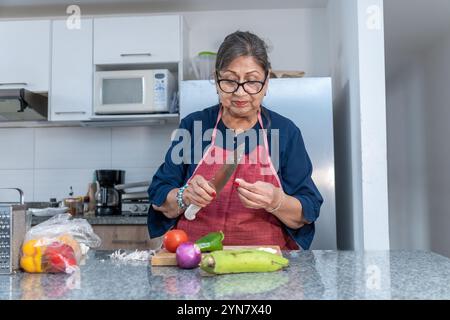 Una donna sta tagliando verdure su un bancone. Indossa un grembiule rosso e ha un coltello in mano Foto Stock