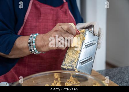 Primo piano delle mani di una donna adulta che grattugia la banana verde su una grattugia per una ricetta dell'America Latina proveniente dall'Ecuador, dalla Colombia o dall'America centrale Foto Stock