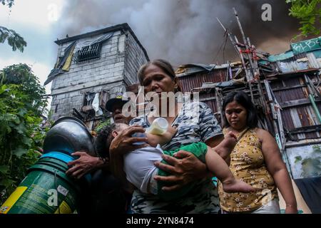 Pechino, Cina. 24 novembre 2024. I residenti evacuano con i loro effetti personali come un enorme incendio inghiottisce un'area di slum a Manila, nelle Filippine, il 24 novembre 2024. Almeno 2.000 famiglie sono rimaste senzatetto dopo che un enorme incendio ha distrutto una comunità residenziale nella capitale filippina il 24 novembre, hanno detto le autorità locali. Crediti: Rouelle Umali/Xinhua/Alamy Live News Foto Stock