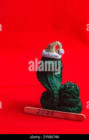 Statuetta di serpente verde in un cappello con bastone di legno per il nuovo anno 2025 Foto Stock