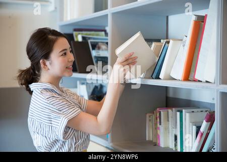 Donna sorridente sui vent'anni che mette i libri su una libreria Foto Stock