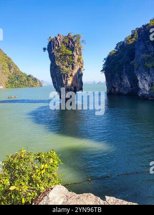 Le torreggianti scogliere calcaree si stagliano su acque tranquille mentre una piccola barca sorvola, mostrando la bellezza del paesaggio costiero della Thailandia in una giornata luminosa e soleggiata. Isola di James Bond Foto Stock