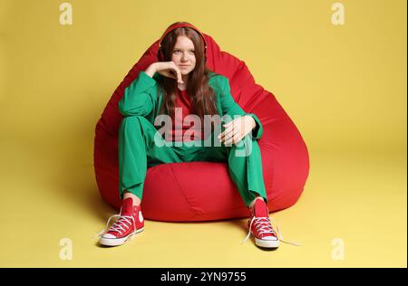 Adolescente dai capelli rossi con cuffie sedute su beanbag su sfondo dorato Foto Stock