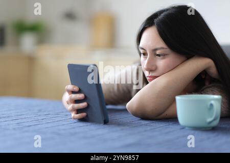 Donna asiatica seria che legge eBook in cucina a casa Foto Stock