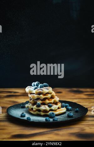 Waffle belgi con mirtilli, cosparsi di zucchero a velo. Waffle con frutti di bosco su sfondo nero su un tavolo di legno. Foto di alta qualità Foto Stock