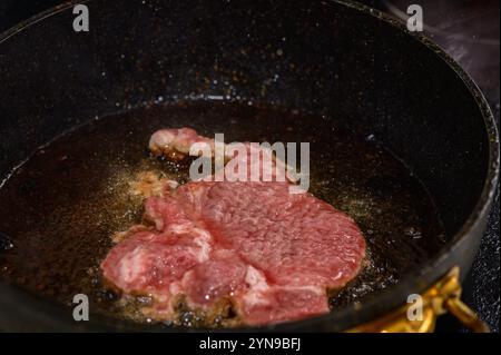 Una succulenta bistecca in olio caldo, riempiendo la cucina con appetitosi aromi durante una calda serata. Foto Stock