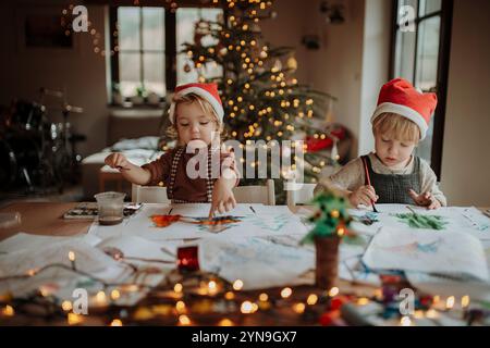 Fratelli che preparano biglietti natalizi per la famiglia. I bambini dipingono quadri per Babbo natale o realizzano decorazioni natalizie con acquerelli. Foto Stock